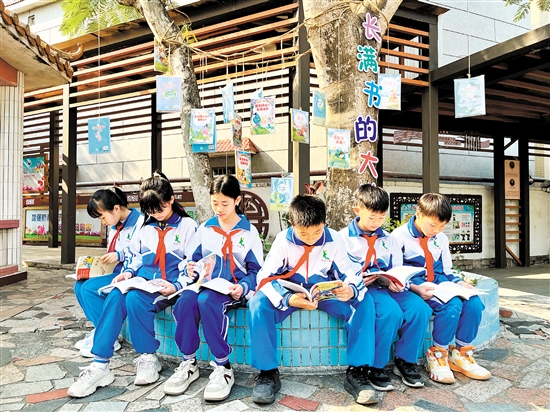 龍口鎮(zhèn)協(xié)華小學(xué)學(xué)生圍坐在“長(zhǎng)滿書的大樹”下捧書共讀，成為該校一道亮麗的風(fēng)景線。